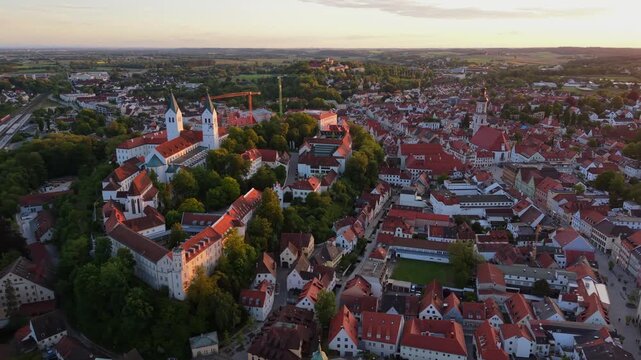 Drone aerial view over Freising, Bavaria, Germany, shows Domberg with Freising Cathedral, St. George Church, and Residenzturm rising above the historic old town skyline during a warm summer sunset