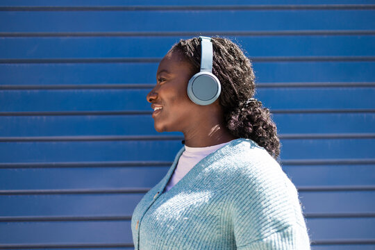 African woman with headphones smiling against blue wall