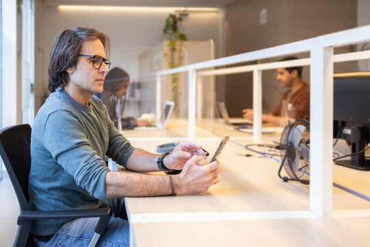 Professional using smartphone at desk in modern coworking