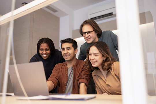 Diverse coworking team collaborating around laptop in office