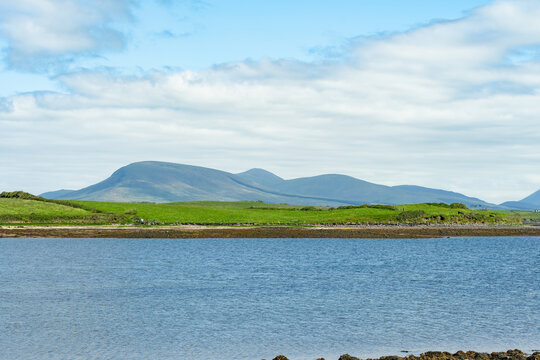 A small sailboat floats in calm water in Clew Bay, County Mayo, Ireland, with green hills beyond. A serene coastal landscape on Irelands west coast.