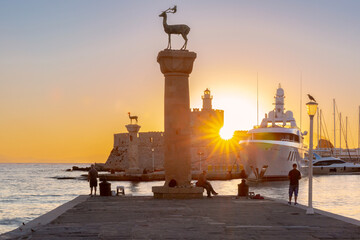 Sunrise view of Mandraki Harbor in Rhodes with deer statues, yachts and calm sea water near the historic waterfront. © Kavalenkava