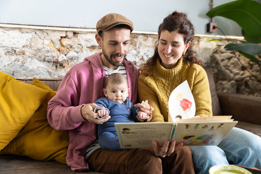 Happy new parents reading with newborn baby at home