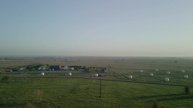 Aerial view of satellite dish station and telecommunication complex in a field. Earth space communication, global network technology and infrastructure drone footage.