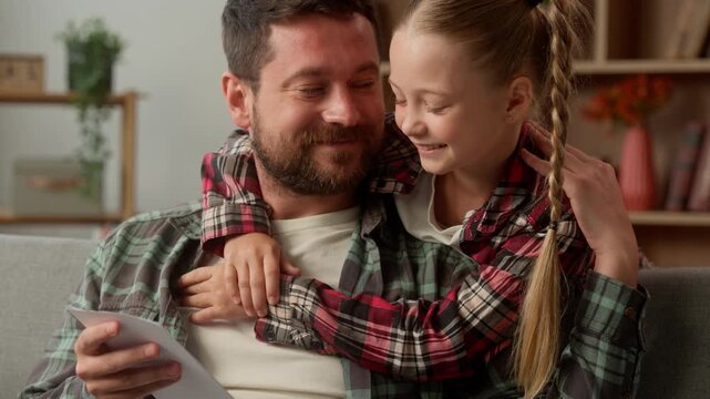 Happy loving Caucasian daughter child hug father dad at home read present card little girl kid embracing parent male man schoolgirl smile guy gift family bonding holiday celebrate together birthday