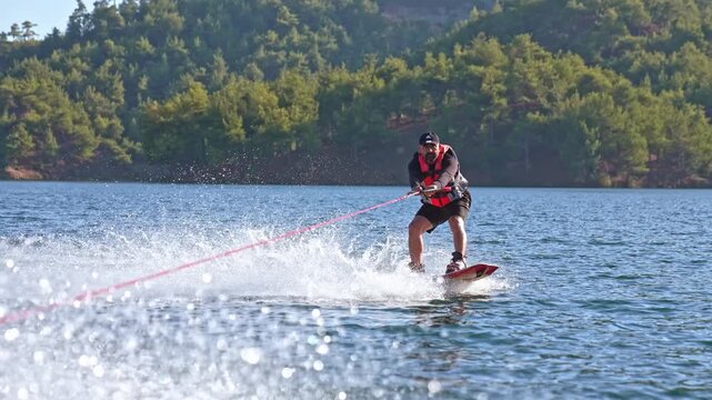 Dynamic shot of a water skier gliding across a calm lake near a forest shoreline. Summer recreation, outdoor adventure, water sports and vacation lifestyle in a scenic natural setting.