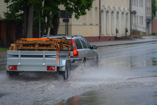 Car with trailer driving through flooded urban street during heavy rainstorm