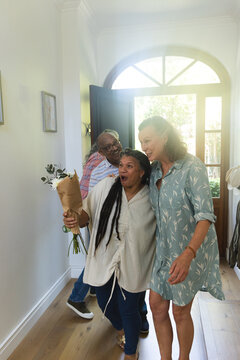 Diverse friends gathering near arched front door at home, holding wrapped bouquet and hugging