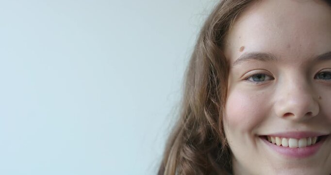 Female reacting to camera, shifting expression from neutral to warm smile in room, copy space