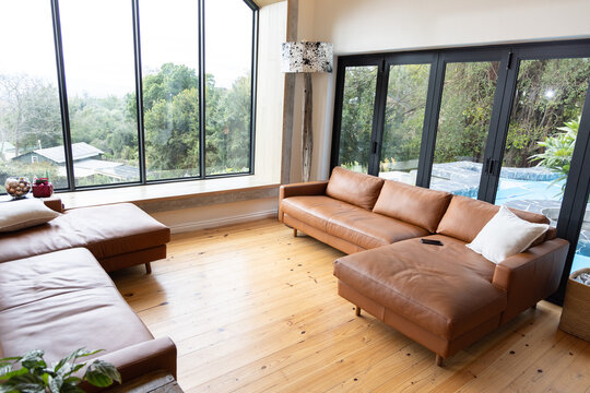 Tan leather sofa chaise sitting on wood floor by windows, phone resting, lamp standing, copy space