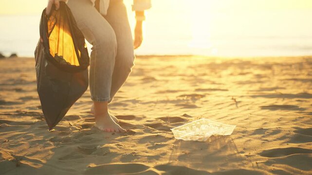 Dedicated volunteer collecting plastic litter from sandy beach during sunset, supporting community service, environmental responsibility, and cleaner public spaces