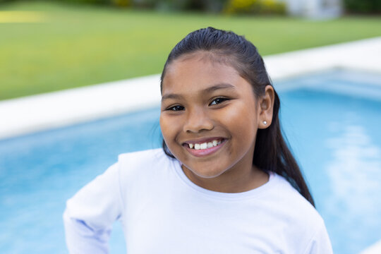 African American child smiling, standing at home pool edge in white longsleeve top and stud earring