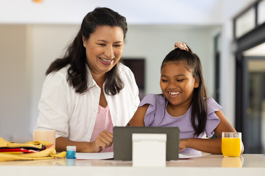 African American mother and child smiling, using tablet on stand at kitchen counter