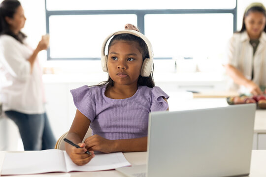 Diverse family with African American child studying on laptop in kitchen wearing white headphones