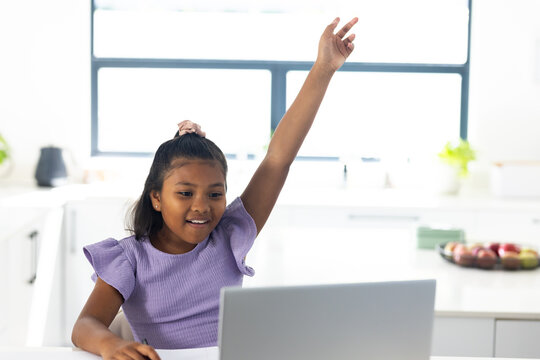 African American girl child sitting at kitchen facing laptop, in purple top, bowl of fruit nearby