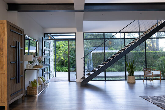 Metal floating staircase angling across open-plan foyer, framing full-height glass wall and armoire