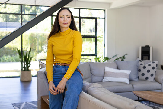 Adult woman sitting on sectional sofa wearing mustard turtleneck and jeans in modern living room