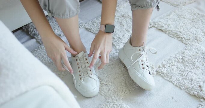 Reaching down, adult is pulling aglet, tightening, tying white sneaker laces on rug to secure shoe