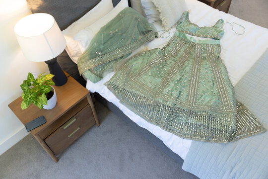 Sea-green beaded sequined lehenga with top and dupatta is lying on bed near lamp and plant