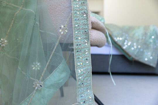 Sheer embroidered teal textile is draping over metal chair and mattress edge, showing beadwork