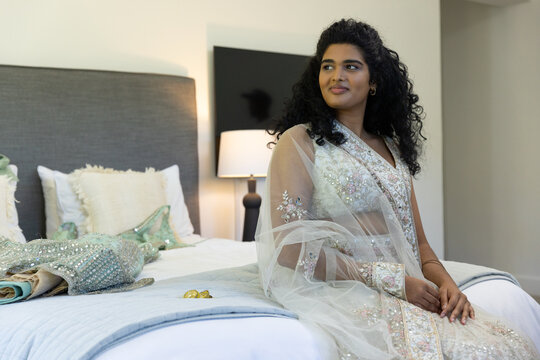 Indian woman sitting on bed wearing embroidered lehenga and dupatta, lamp glowing, copy space