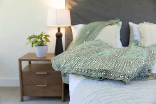 Heavy beaded pale green sequin garment is draping across bed near oak nightstand, soft lamp light