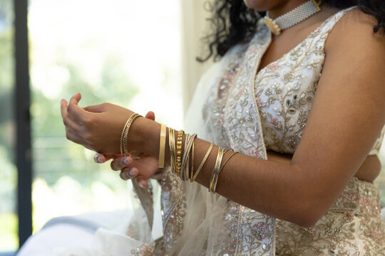 Indian woman sitting near bright window adjusting gold bangles wearing choker and sheer dupatta