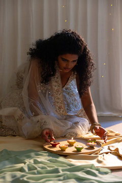 Indian woman kneeling, arranging colorful cup sweets on wooden board in lehenga and bangles at home