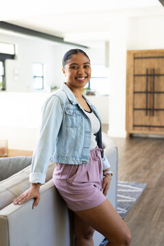 Adult African American woman standing, leaning on sofa, smiling, showing kitchen counter and rug
