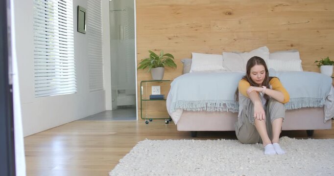 Woman sitting at foot of bed in bedroom, wearing mustard top, glancing toward doorway, copy space