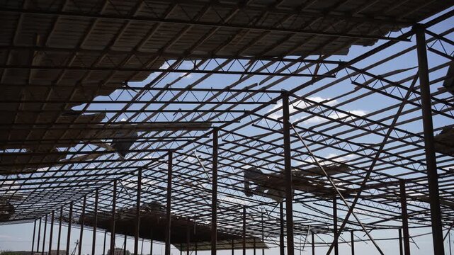 Damaged roof frame with torn metal sheets and rusty beams. Abandoned building concept.