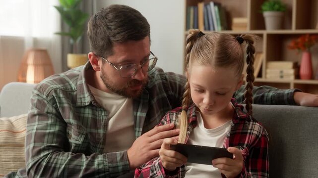 Upset Caucasian dad man touching talk little girl daughter addict playing game worried male daddy child family problem at home bad behavior kid ignore father guy online use mobile phone device gadget