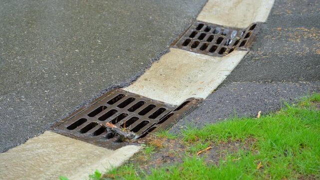 Street drain with water flowing into it during rainfall. 