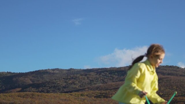 Gymnastics girl practices juggling clubs outdoors against a bright blue sky and distant hills