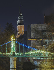 Podświetlony Most Groszowy w Opolu nocą. Zabytkowy Zielony Mostek nad Młynówką z odbiciem w wodzie i wieżą w tle. Romantyczna iluminacja miejska. © Henryk Niestrój