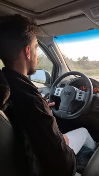 Driving car roadtrip young man commuting during golden hour on a winding road, interior view from back seat.