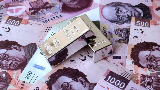A silver bar, white metal against a backdrop of Mexican money, as a concept for the sales market. A silver bar as a background for your design