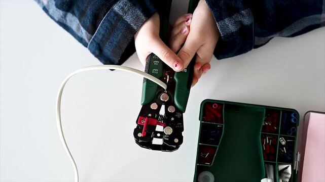 Close up of student hands using wire stripper tool on white desk with crimper and cables nearby, detailed STEM skills practice and accessible home electronics workshop for self directed engineering