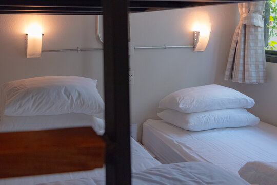 An interior photograph of a cozy and modern hostel dormitory room featuring a sleek black metal bunk bed frame with a striking red ladder and top railing. The lower bed is neatly made with crisp white