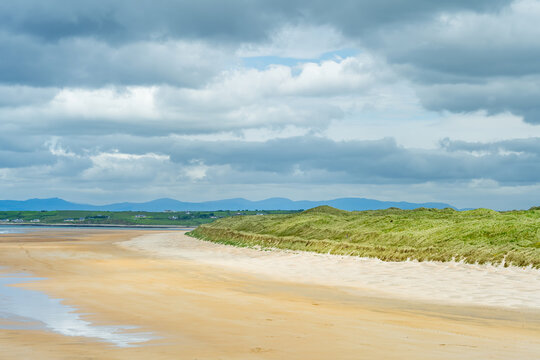 Wide view of Tullan Strand with sand dunes under dramatic clouds on Irelands Atlantic coast. A coastal landscape highlighting empty beach scenery and wild weather.
