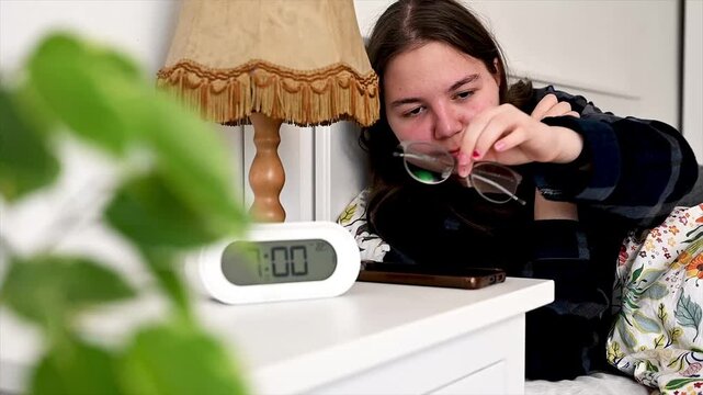 Teenage girl relaxing in bed browsing content on handheld device during quiet morning, peaceful leisure moment before starting school day preparation showing authentic generation z digital morning