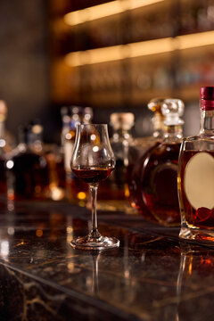 Glass of bourbon placed among premium drinks arranged at bar counter.