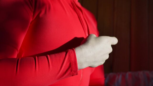 Zipper garment reveal woman slowly unzips her red bodysuit while standing against a rustic wooden wall in soft natural light