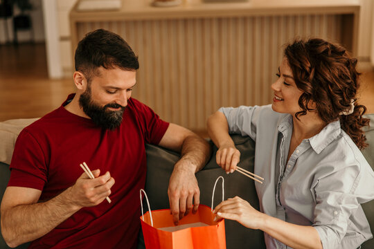 Couple enjoying casual takeout dinner with chopsticks at home