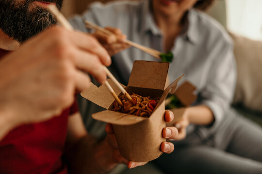 Couple eating takeout noodles with chopsticks at home