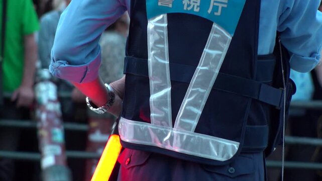JAPAN : Back view of a Japanese police officer standing on a city street during a patrol. Officer in uniform watching public safety and security. Slow motion shot.