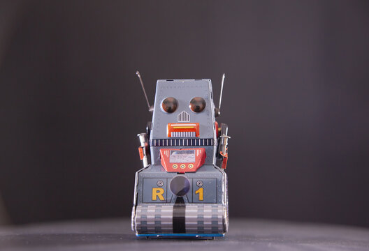 Classic vintage tin robot toy with orange and gray metallic finish on neutral . Retro collectible features antennas and tracked wheels. Nostalgic childhood toy representing 1950s science fiction era.
