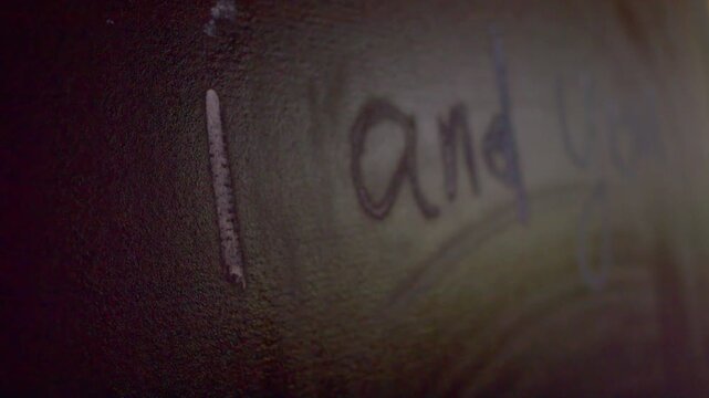 A hand erases the words "i and you" written in chalk from a board with a rag.