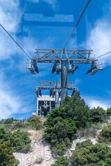 Fototapeta premium View from a cable car cabin approaching a massive metal support tower and station on top of a green mountain.
