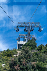 Fototapeta premium View from a cable car cabin approaching a massive metal support tower and station on top of a green mountain.